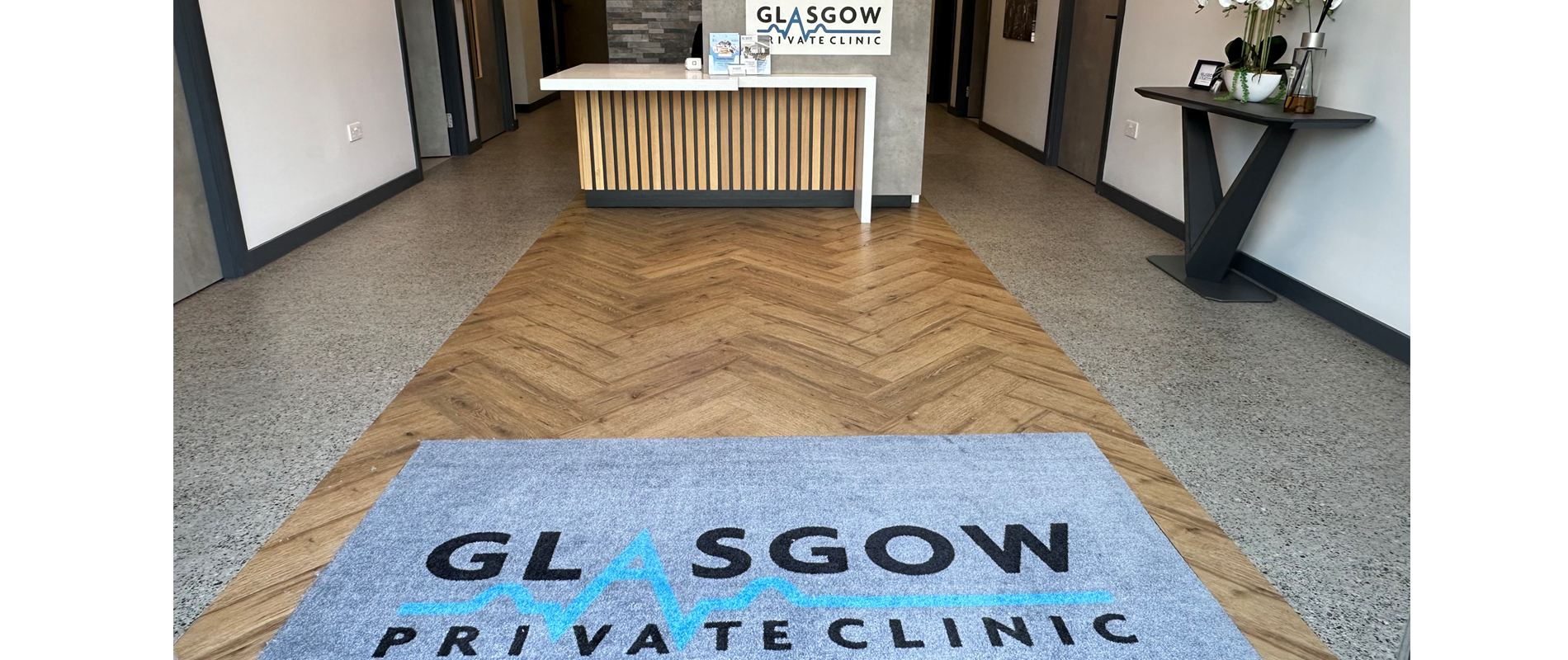 The clinic reception — herringbone oak runner, stone counter and the illuminated Glasgow Private Clinic lightbox